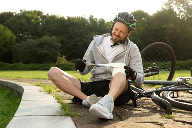Man applying bandage onto his knee near bicycle outdoors
