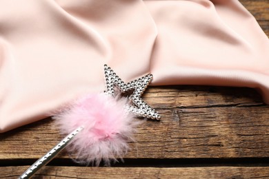 Beautiful silver magic wand with feather and pink fabric on wooden table, closeup