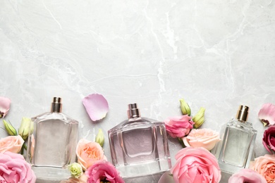 Flat lay composition of different perfume bottles and flowers on light grey marble background, space for text