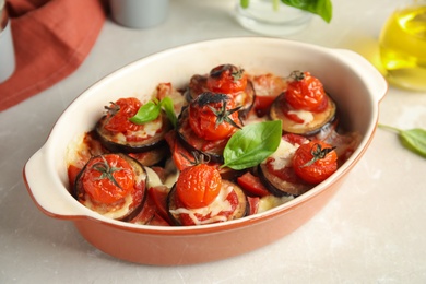 Photo of Baked eggplant with tomatoes, cheese and basil in dishware on light table, closeup