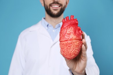 Doctor with model of heart on light blue background, closeup. Cardiology concept