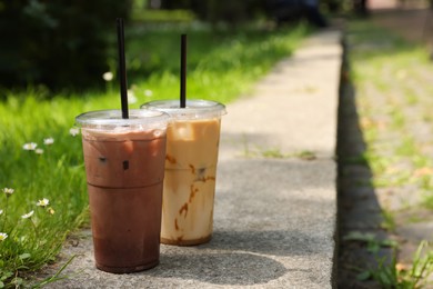 Takeaway plastic cups with cold coffee drinks near green grass outdoors, space for text