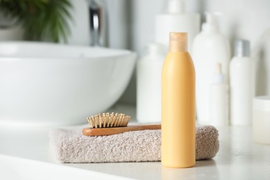 Bottle of shampoo, towel and wooden hairbrush near sink on bathroom counter, space for text