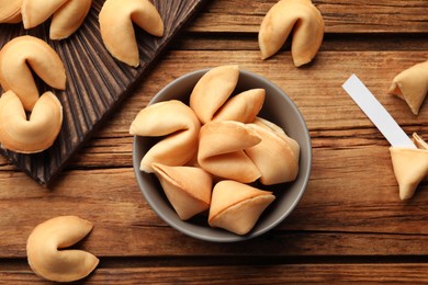 Photo of Tasty fortune cookies and paper with prediction on wooden table, flat lay