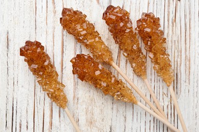 Sticks with sugar crystals on white wooden table, flat lay. Tasty rock candies