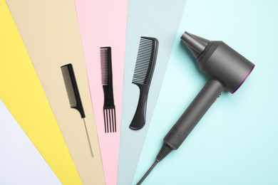 Hair dryer and different combs on color background, flat lay. Professional hairdresser tool