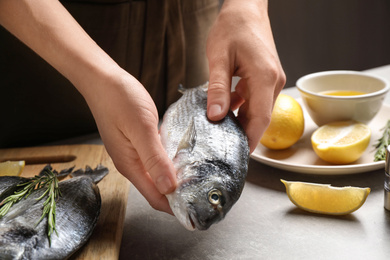 Woman holding dorada fish over grey table, closeup