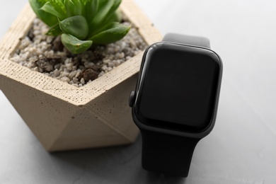 Stylish smart watch and plant on grey table, closeup