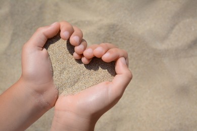 Child holding sand in hands outdoors, closeup. Fleeting time concept