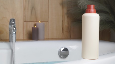 Beige bottle of bath foam and candles on tub indoors, space for text