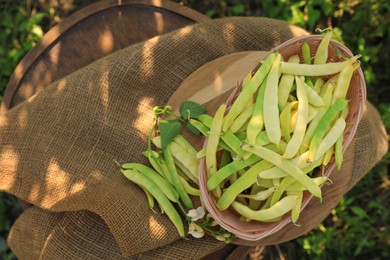 Wicker basket with fresh green beans on wooden chair in garden, top view
