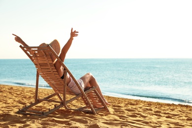 Woman relaxing on deck chair at sandy beach. Summer vacation