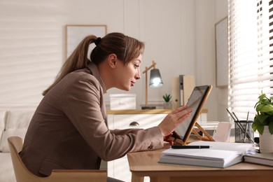 Young woman with poor posture using tablet at table indoors