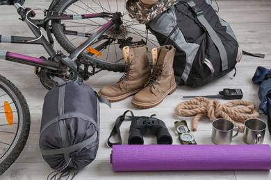 Sleeping bag, bicycle and set of camping equipment on wooden floor
