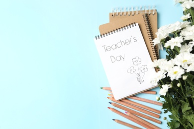Notebook with phrase Teacher's Day and beautiful white flowers on light blue background, flat lay. Space for text