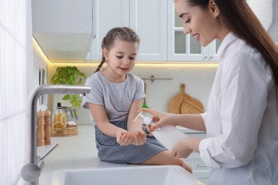 Mother and daughter washing hands with liquid soap together in kitchen