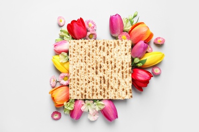 Tasty matzo and flowers on light background, flat lay. Passover (Pesach) celebration