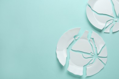 Two broken ceramic plates on light blue background, flat lay. Space for text