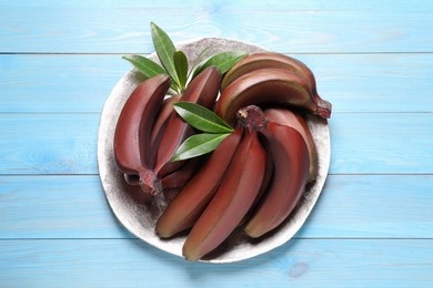 Tasty red baby bananas on light blue wooden table, top view