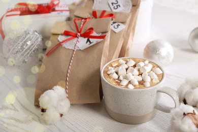 Photo of Christmas gifts, cup of marshmallow cocoa and festive decor on white wooden table. Creating Advent calendar