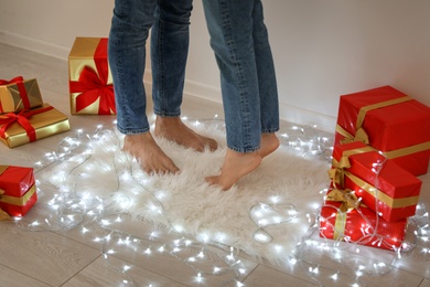 Young couple standing on rug near Christmas lights and gift boxes, closeup