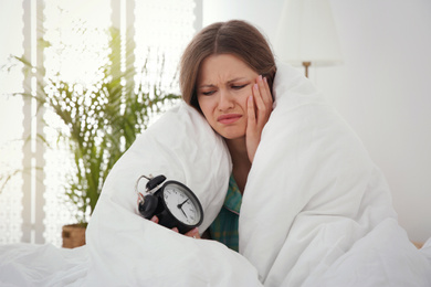 Sleepy young woman with alarm clock at home in morning