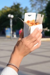 Photo of Woman holding paper box of takeaway noodles outdoors, closeup. Street food