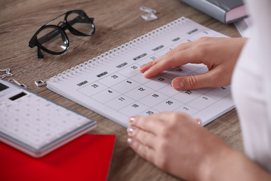 Photo of Woman with calendar at wooden table, closeup
