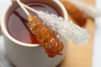 Sticks with sugar crystals and cup of tea on table, closeup