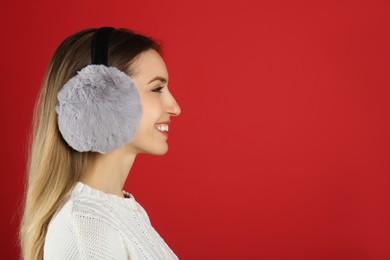 Happy woman wearing warm earmuffs on red background, space for text