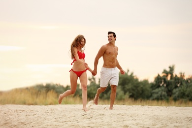 Happy young couple running together on sea beach at sunset