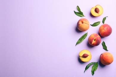 Fresh ripe peaches and green leaves on violet background, flat lay. Space for text