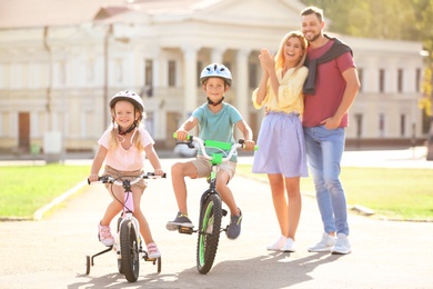 Photo of Happy parents teaching children to ride bicycles outdoors