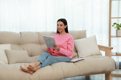 Young woman coloring antistress page on sofa in living room