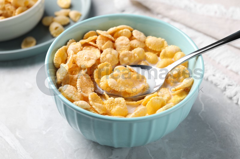 Spoon in bowl with tasty cornflakes and milk on light grey table
