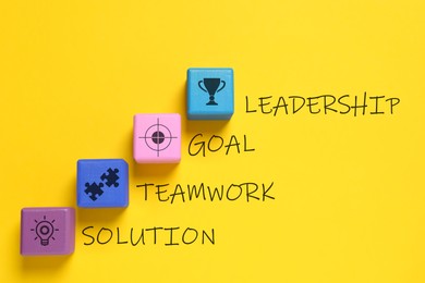 Colorful cubes with different images and words Leadership, Goal, Teamwork and Solution on yellow background, flat lay