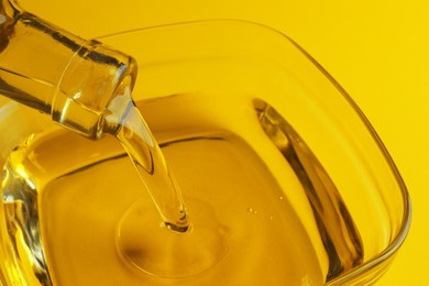 Photo of Pouring cooking oil from bottle into bowl on yellow background, closeup