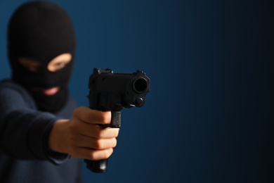 Man in mask holding gun against dark blue background, focus on hand. Space for text