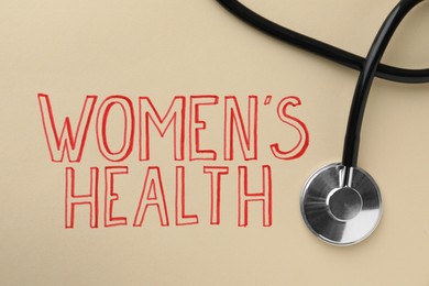 Words Women's Health and stethoscope on beige background, top view