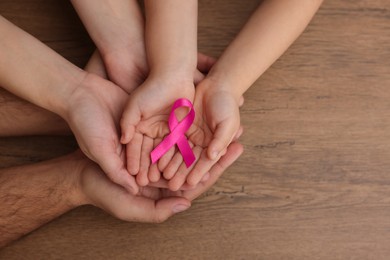 Family holding pink ribbon on wooden background, top view with space for text. Breast cancer awareness