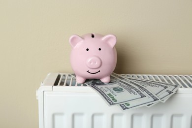 Photo of Piggy bank and dollar banknotes on heating radiator against beige background