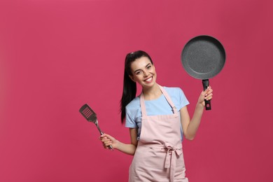 Photo of Housewife with frying pan and spatula on pink background. Space for text