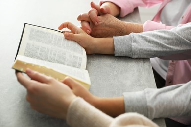 Boy and his godparents reading Bible together at grey table, closeup