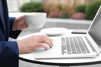 Photo of Businessman with laptop and coffee in outdoor cafe, closeup. Corporate blog