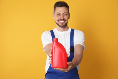 Man showing motor oil against orange background, focus on container