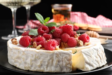 Brie cheese served with raspberries and walnuts on black plate, closeup