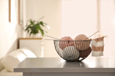Yarn balls and knitting needles in metal basket on grey table indoors, space for text. Creative hobby