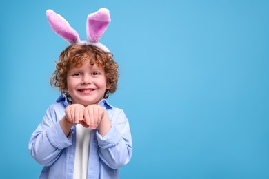 Photo of Portrait of happy boy wearing bunny ears headband on light blue background. Space for text. Easter celebration