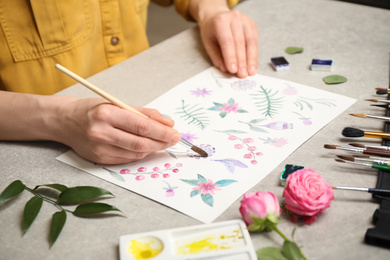 Woman painting flowers with watercolor at grey stone table, closeup
