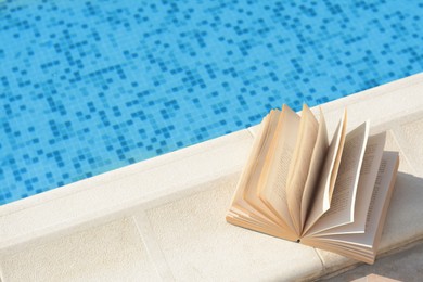 Photo of Open book on swimming pool edge during sunny day, above view. Space for text